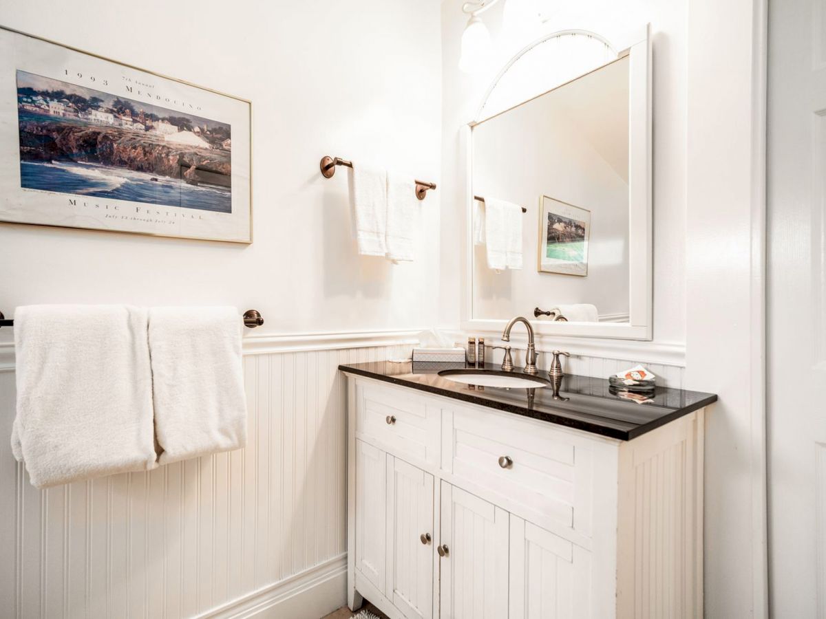 A neatly arranged bathroom features a white vanity with a black countertop, a mirror, towels, and a framed picture on the wall ending the sentence.