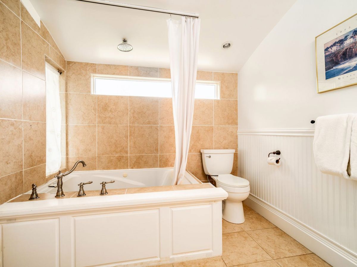 A bathroom features a bathtub with a shower curtain, a toilet, and a towel rack with two towels, all in a well-lit, tiled setting.