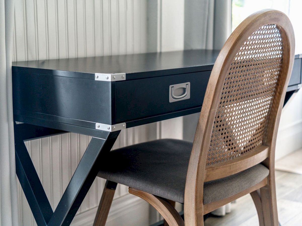 A small black desk with a drawer and a wooden chair with a woven backrest placed in front of it.