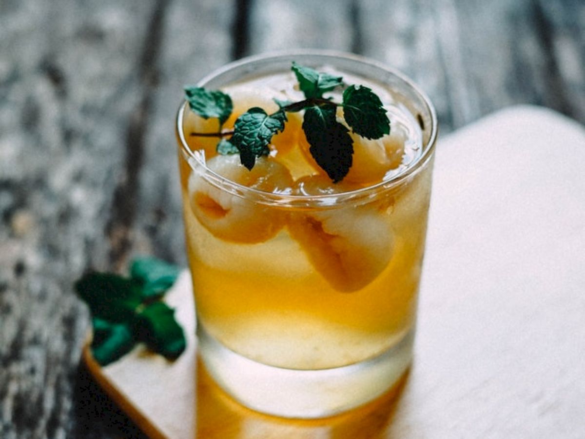 A refreshing drink garnished with mint leaves and ice, placed on a wooden surface with a rustic background.