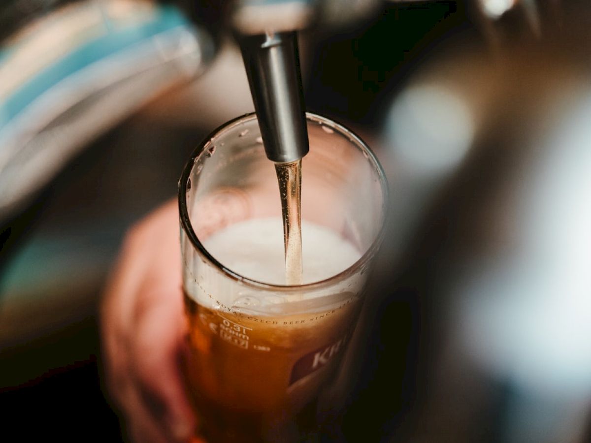 A close-up image of a hand holding a glass, with beer being poured into it from a tap, creating a nice frothy head.