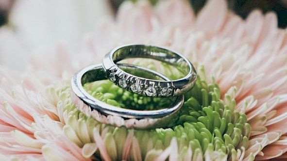 Two wedding rings are placed on a pink flower with green center, likely symbolizing marriage or engagement.