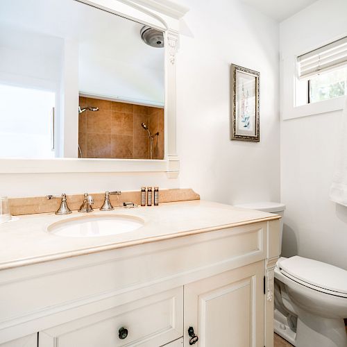 A clean white bathroom with a sink, mirror, toilet, and towels on the wall next to a window with blinds, ending the sentence.