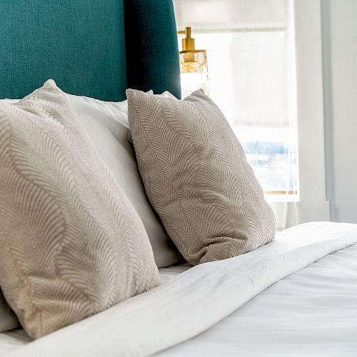 The image shows a bed with a teal-colored headboard and three light beige pillows neatly arranged on white bed linens.