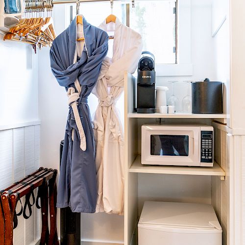 The image shows a small closet space with a microwave, mini-fridge, coffee maker, robes hanging, a shelf, and a luggage rack, ending the sentence.