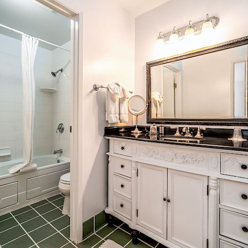 A clean, well-lit bathroom with a white vanity, large mirror, and shower area featuring a bathtub with a white curtain.