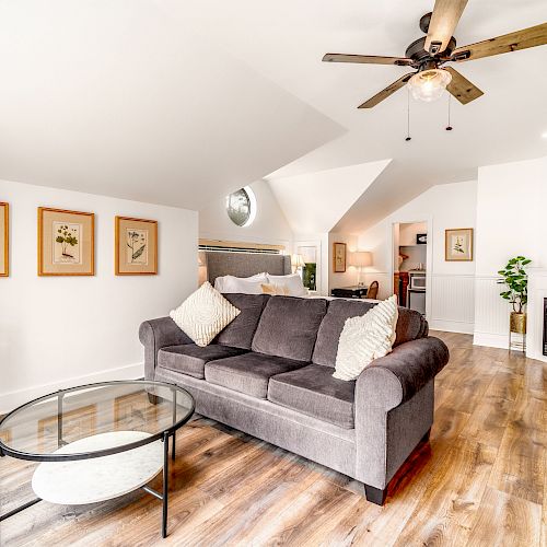 A cozy living space with a gray couch, glass coffee table, ceiling fan, and framed artwork on the wall, hardwood floors, and fireplace.