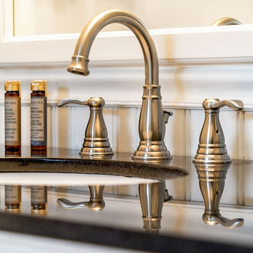 This image shows a bathroom sink with a reflective black countertop, a silver faucet, and three small bottles lined up on the left side.