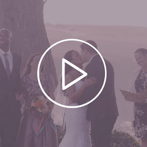 A couple is kissing at their wedding ceremony, surrounded by three people, with a large play button icon in the center of the image.