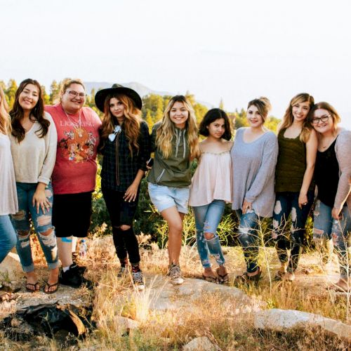 A group of people smiling outdoors, standing on rocky terrain with greenery in the background.