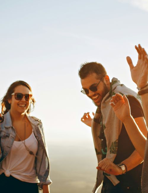 A group of four people enjoying a sunny day, smiling and engaged in conversation, with a clear sky in the background.