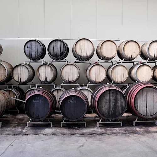 Stacks of wooden barrels aging in a winery warehouse, arranged in rows on racks and shelves.