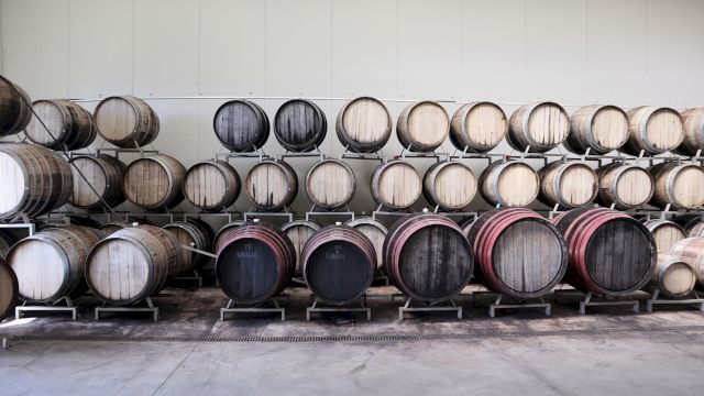 Stacks of wooden barrels aging in a winery warehouse, arranged in rows on racks and shelves.