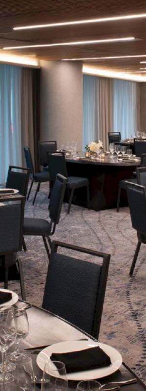 The image shows an elegantly set banquet hall with round tables, black chairs, and dim lighting, ready for an event or reception.