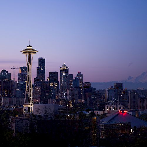 This image shows the Seattle skyline at dusk, featuring the iconic Space Needle and Mount Rainier in the background against a vibrant, twilight sky.