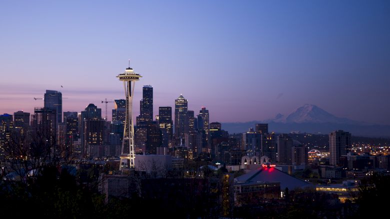 The image shows the Seattle city skyline at twilight, featuring the Space Needle and Mount Rainier in the background.